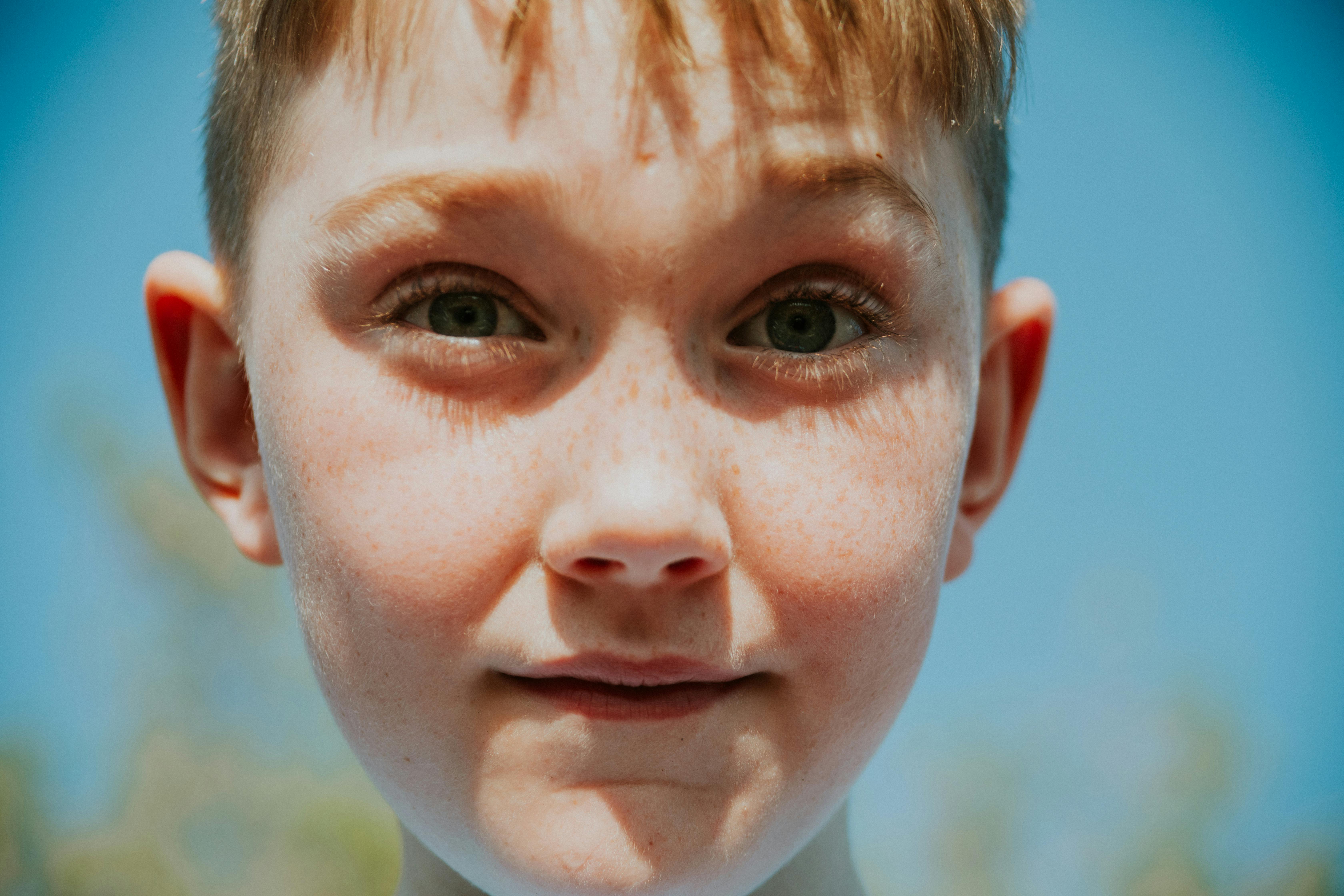 Gratis Una imagen de primer plano de un niño pecoso con ojos expresivos bajo un cielo azul claro. Foto de stock