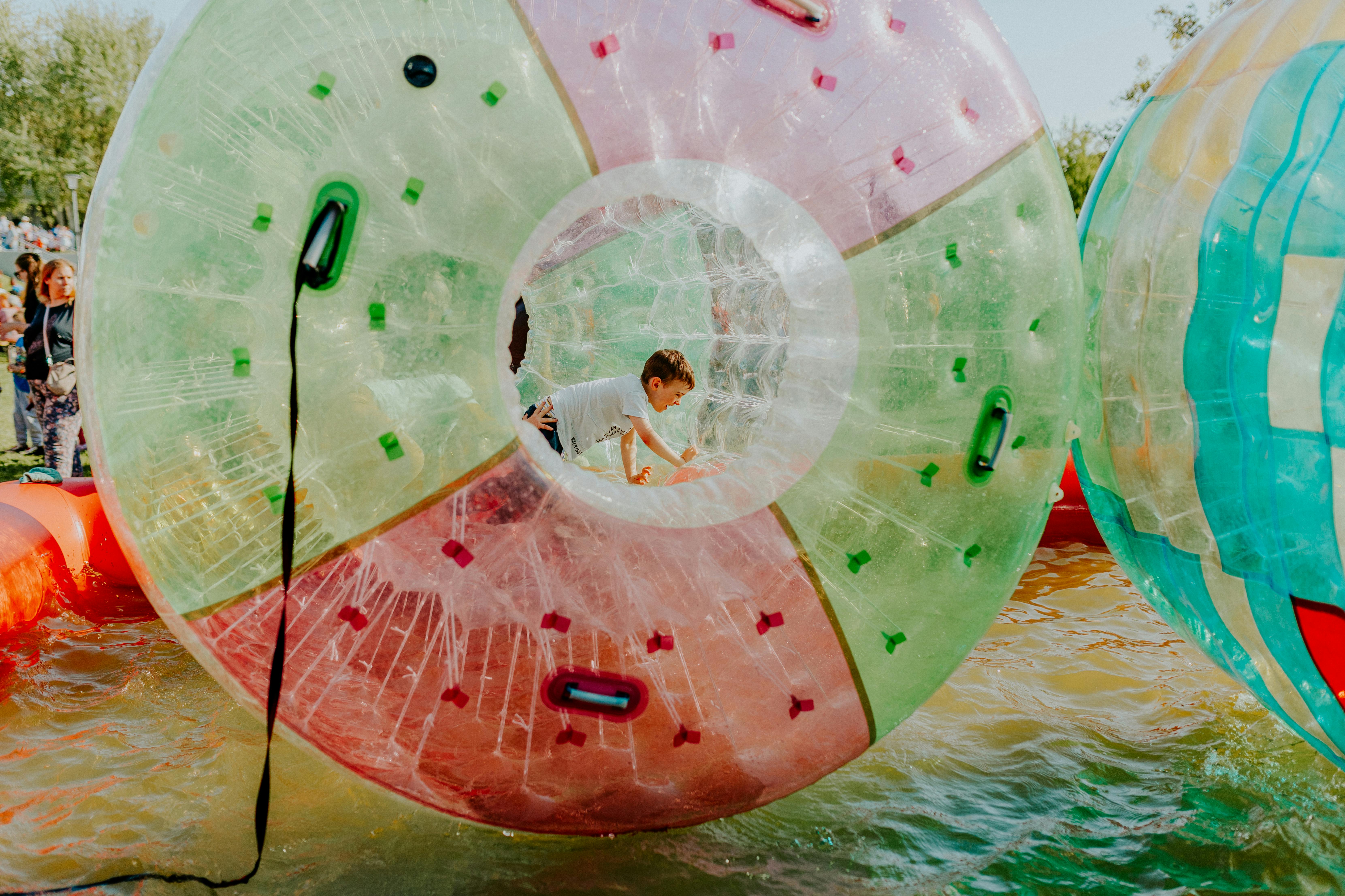 A child enjoys playing inside a vibrant inflatable water ball at an outdoor fair.