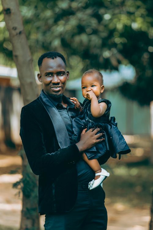 Free A loving father holding his baby daughter, both dressed in black formal wear, outdoors in a park setting. Stock Photo