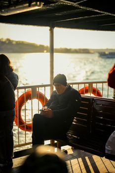 Man sitting on a boat with phone, enjoying a scenic sunny waterfront view.