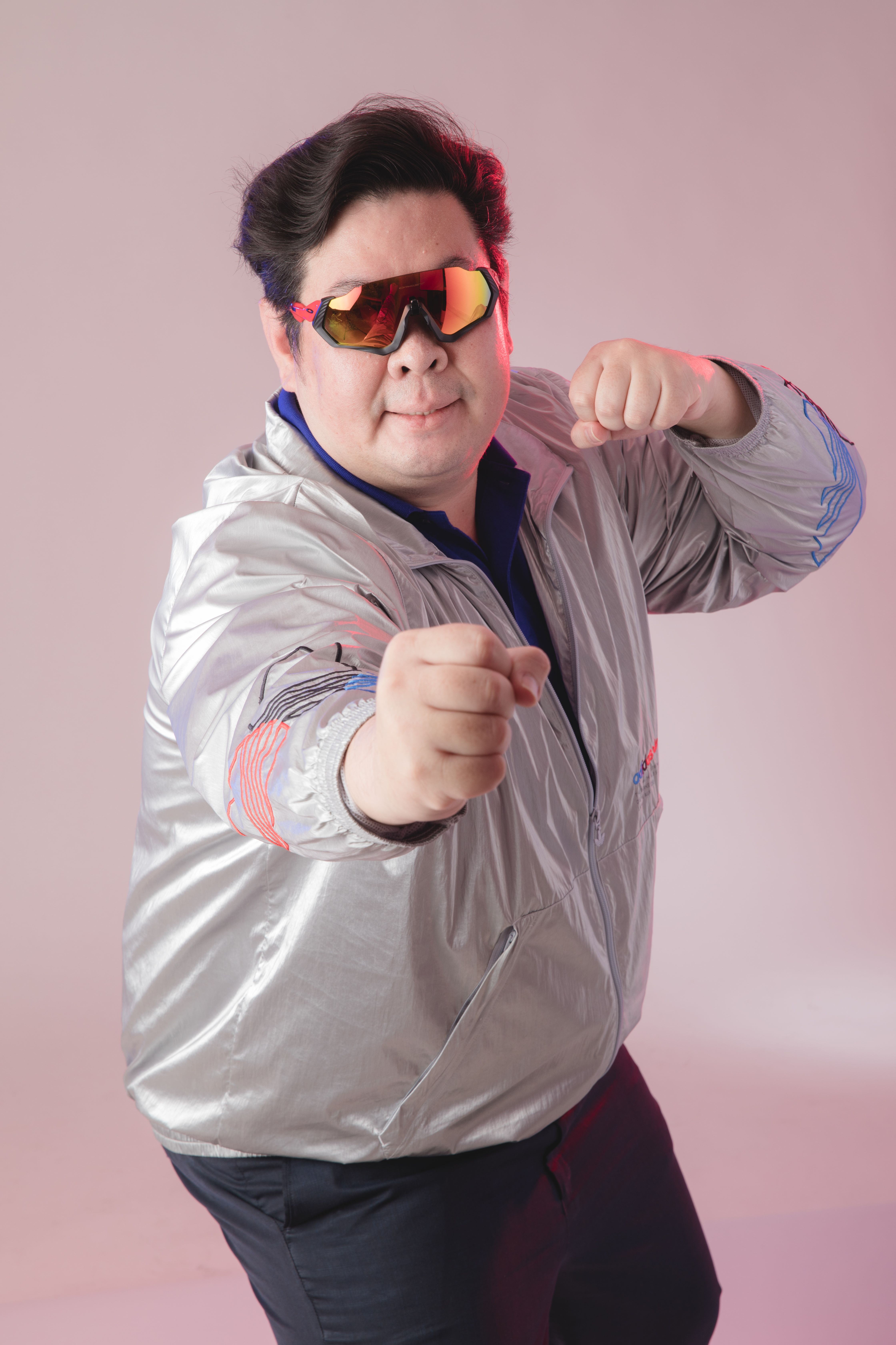 Man posing energetically in a metallic jacket with futuristic sunglasses.
