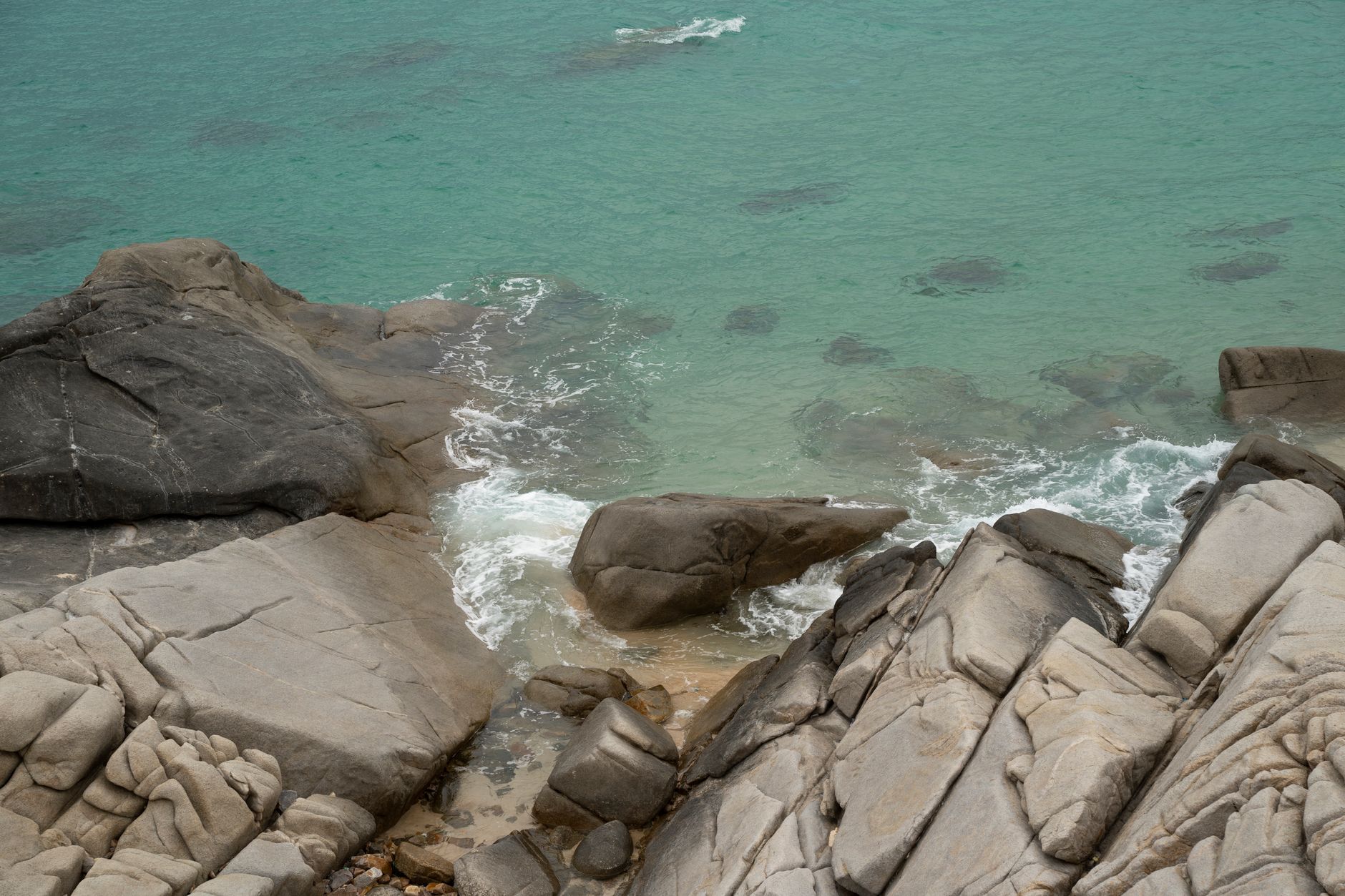 A stunning view of rocky coastline with waves hitting the thick rocks and clear turquoise waters.