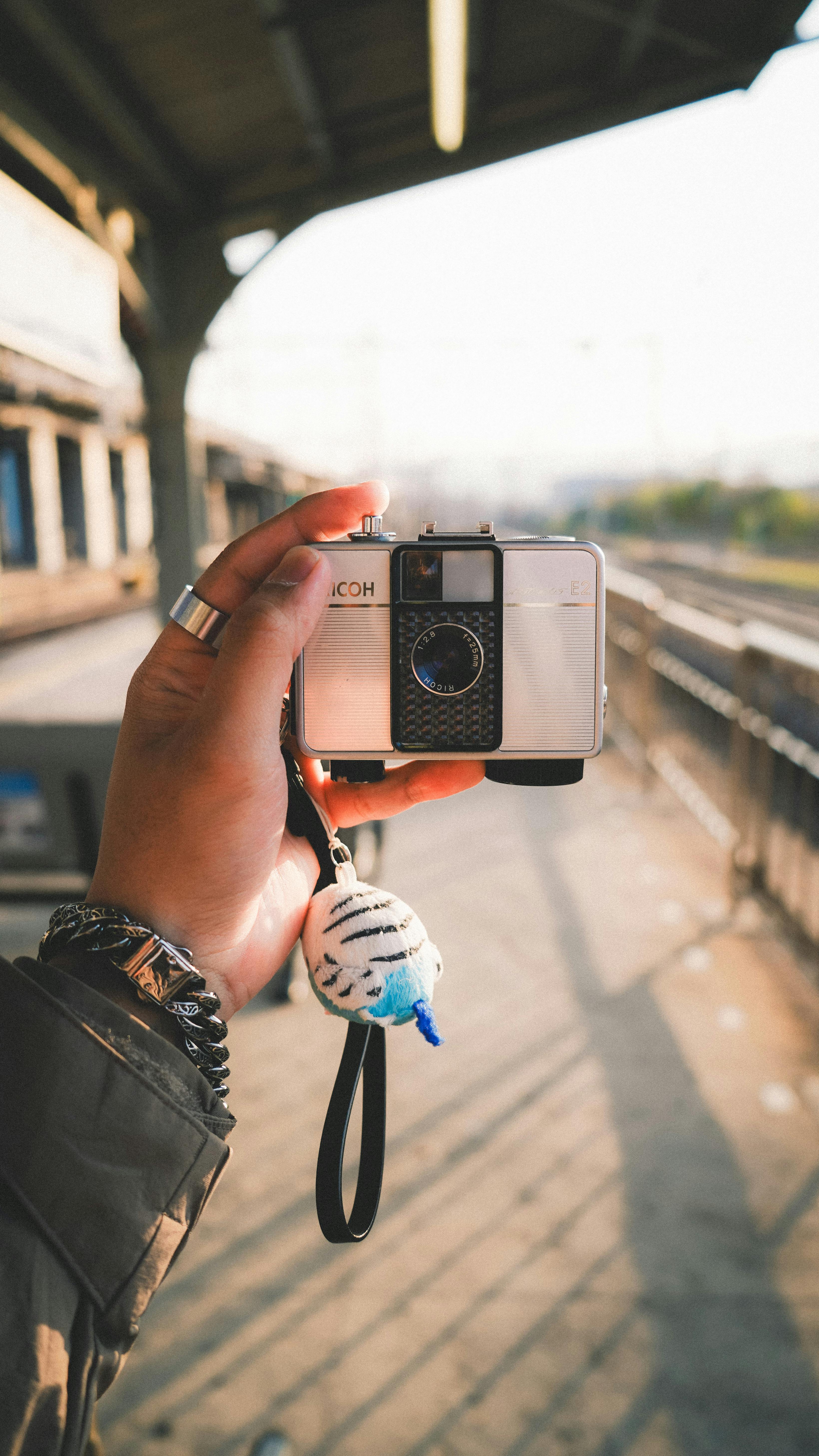 Person holding a vintage camera at a sunlit train station platform, showcasing travel and nostalgia.