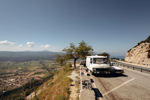 Rustic van parked on mountain road with stunning valley view under a clear sky.