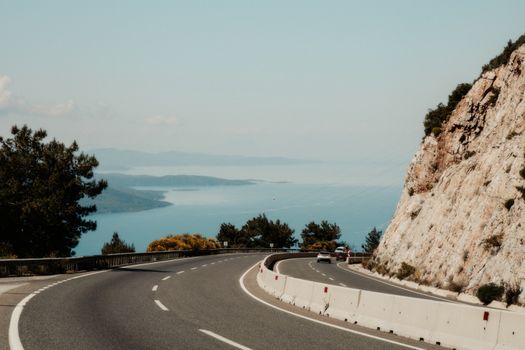 Winding road hugging a rocky cliff with stunning ocean view on a sunny day.