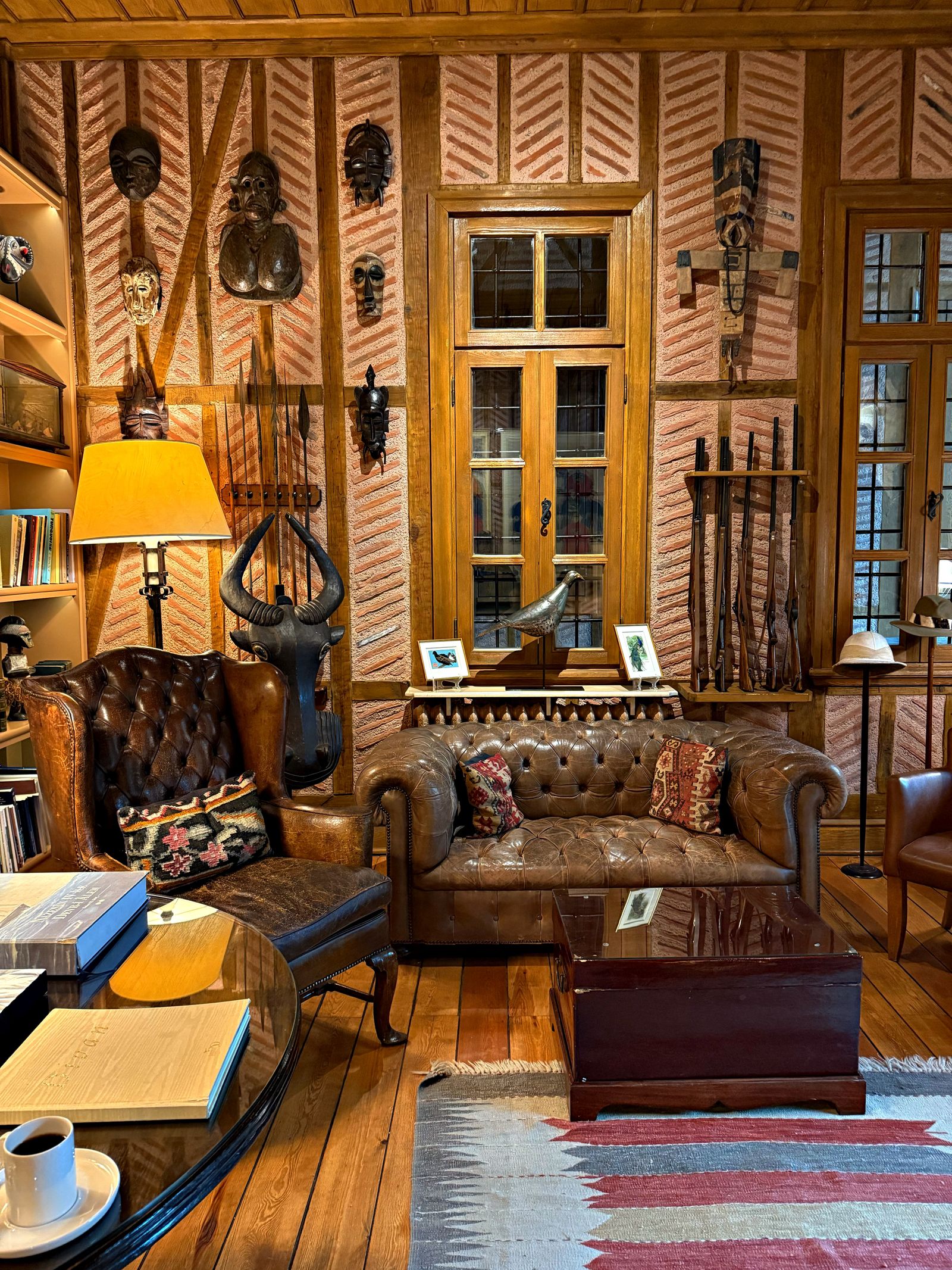 A warmly lit library with rich wood interiors and worn brown leather armchairs.