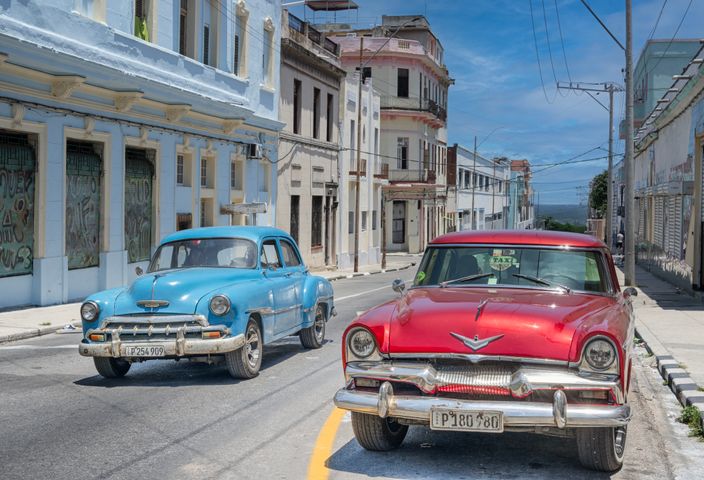 Classic American cars on a bright Havana street, showcasing retro charm and vibrant architecture.