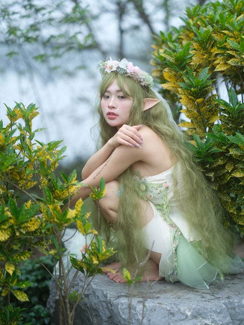 Free A mystical forest fairy with green hair and floral crown surrounded by lush foliage. Stock Photo