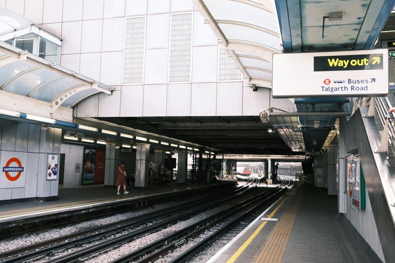 Hammersmith Station platform with train tracks and wayfinding signs, London.