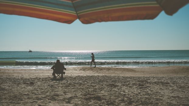 People enjoying a sunny day at the beach under a colorful umbrella by the sea.