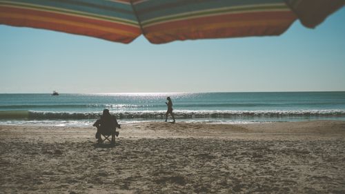Free People enjoying a sunny day at the beach under a colorful umbrella by the sea. Stock Photo