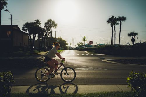 Free Woman cycling near palm trees in a sunny urban environment, depicting an active lifestyle. Stock Photo