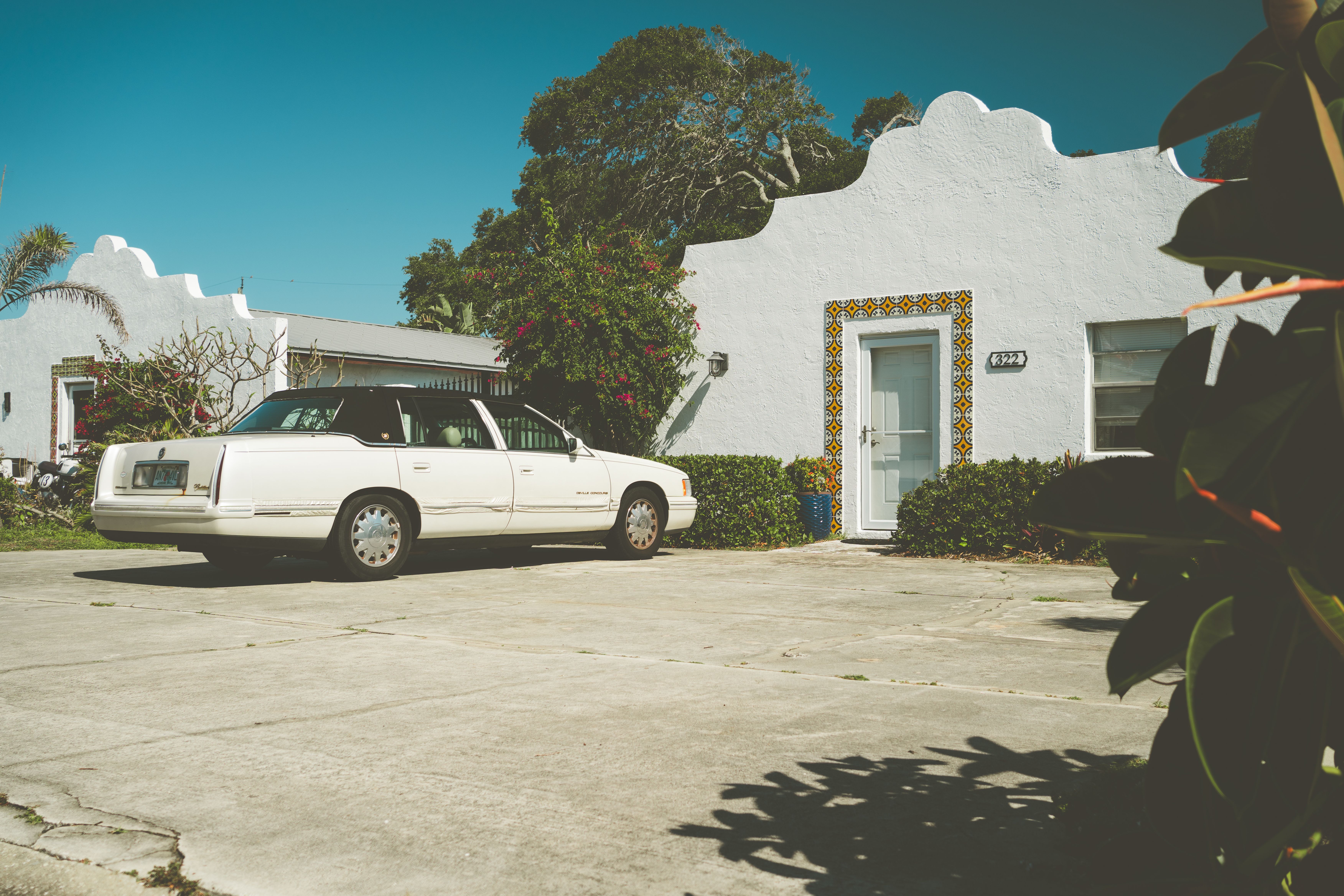 A vintage white sedan parked outside a charming Spanish-style house on a sunny day.