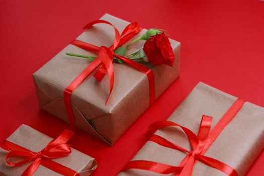 Brown paper gift boxes with red ribbons and rose on a red background, ideal for holiday themes.