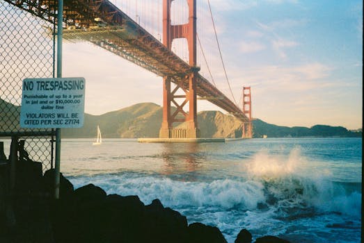 Golden Gate Bridge with waves crashing and a no trespassing sign during sunset.