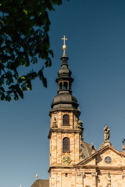 Free A detailed view of a historic church tower with a cross and ornate architecture under a clear blue sky. Stock Photo