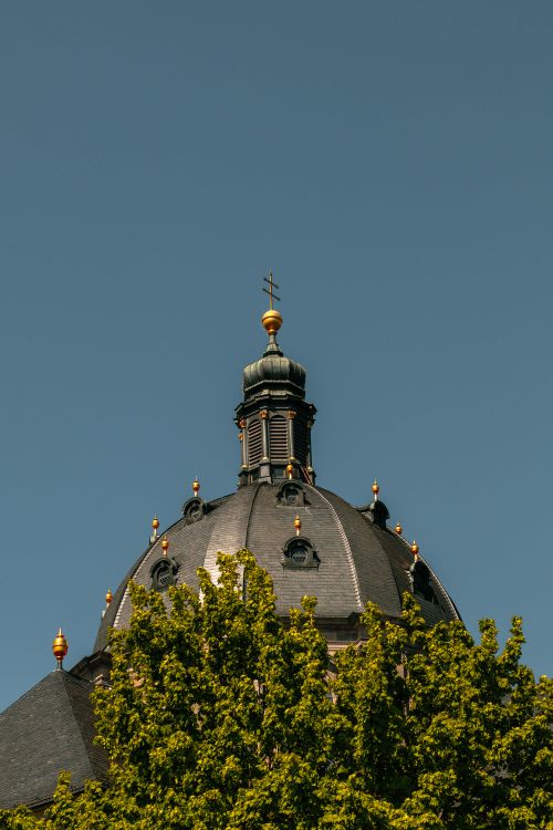 Free Historic church dome with golden elements under a clear blue sky surrounded by trees. Stock Photo