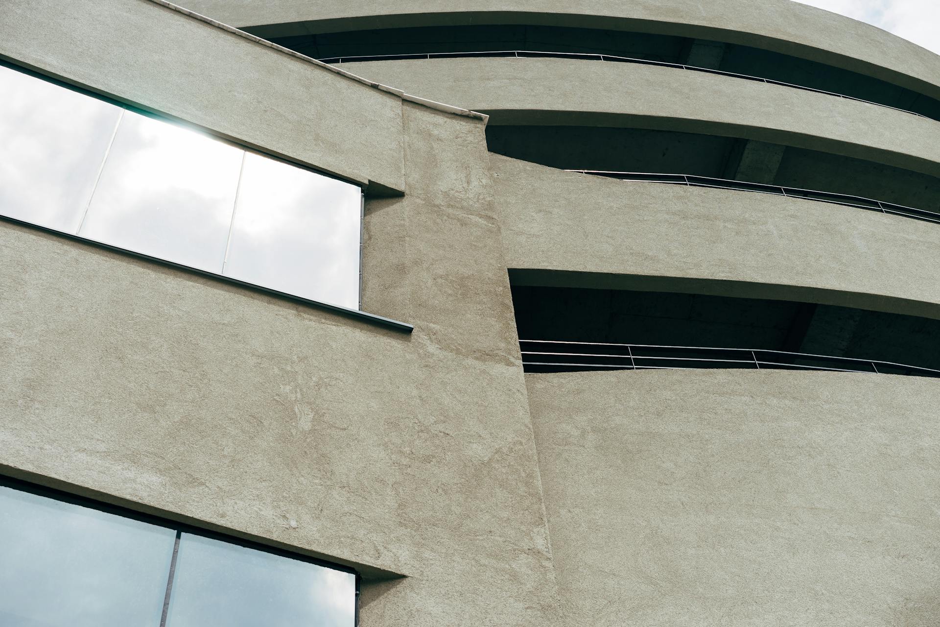 Close-up of a modern brutalist building featuring a rough concrete facade and reflective glass windows.