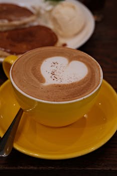 Warm latte with heart art alongside a scrumptious breakfast of pancakes.