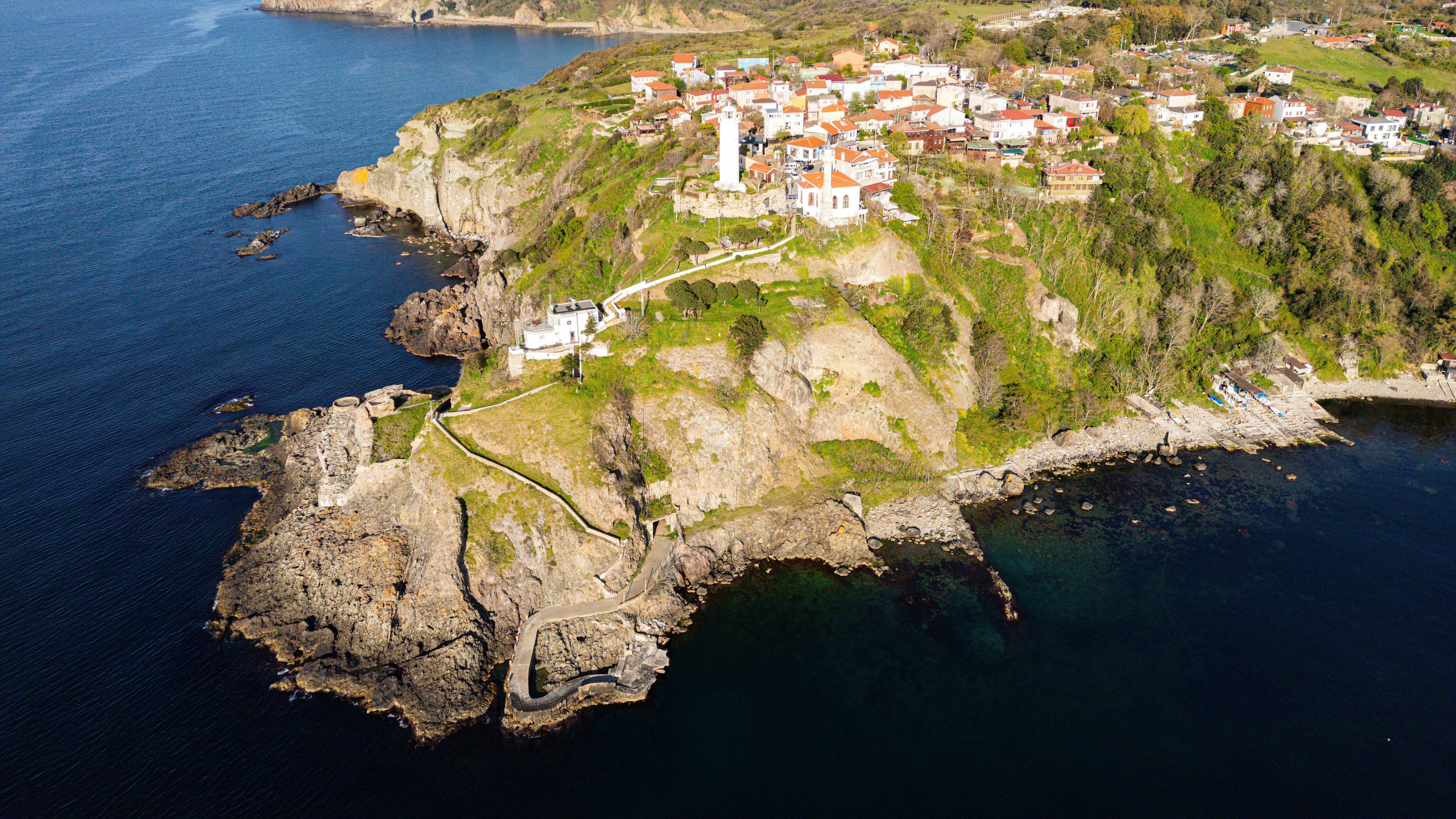 Picturesque aerial view of a coastal cliff village with a lighthouse surrounded by the sea.