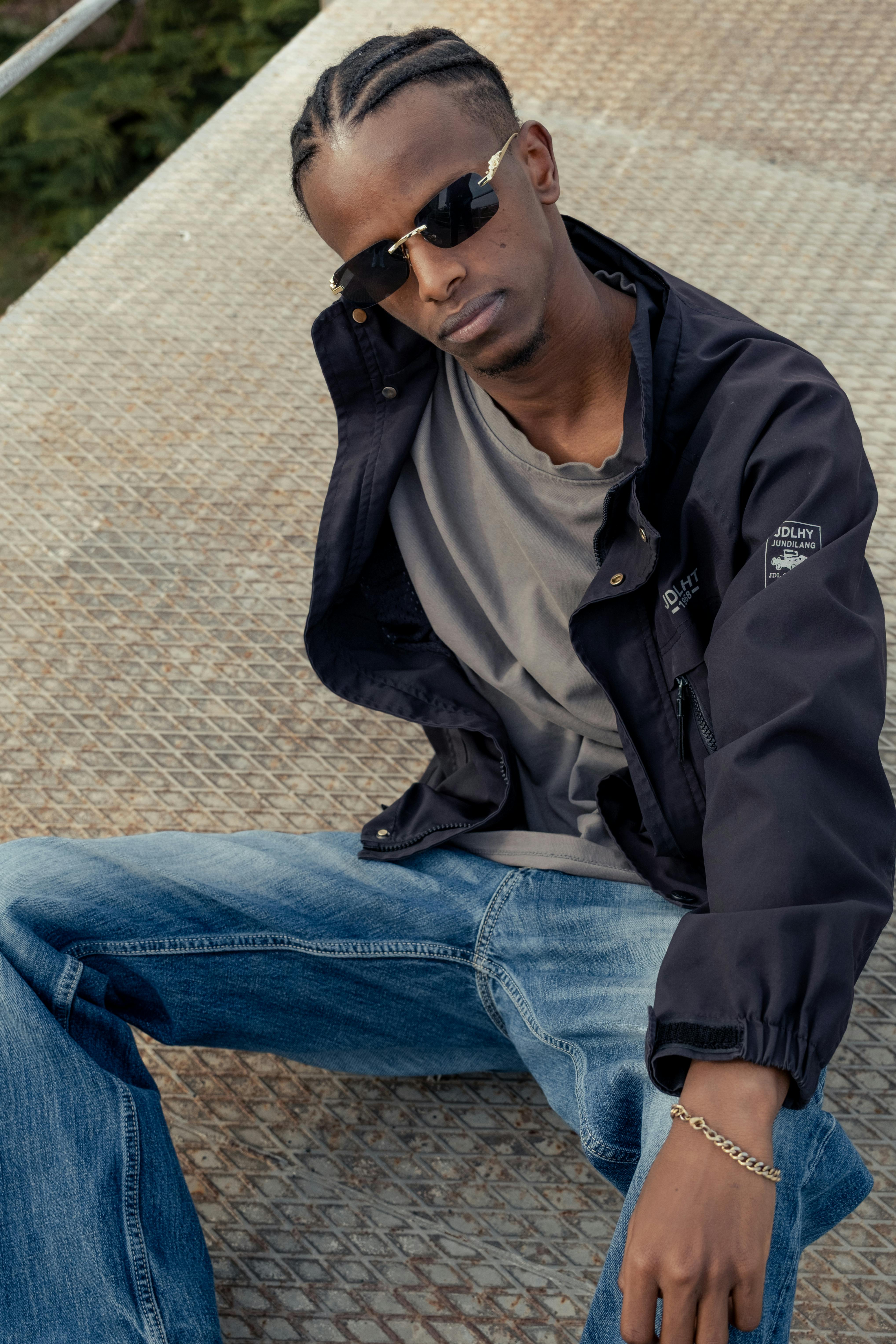 Young man in sunglasses and jacket posing on metallic platform, showcasing urban street style.