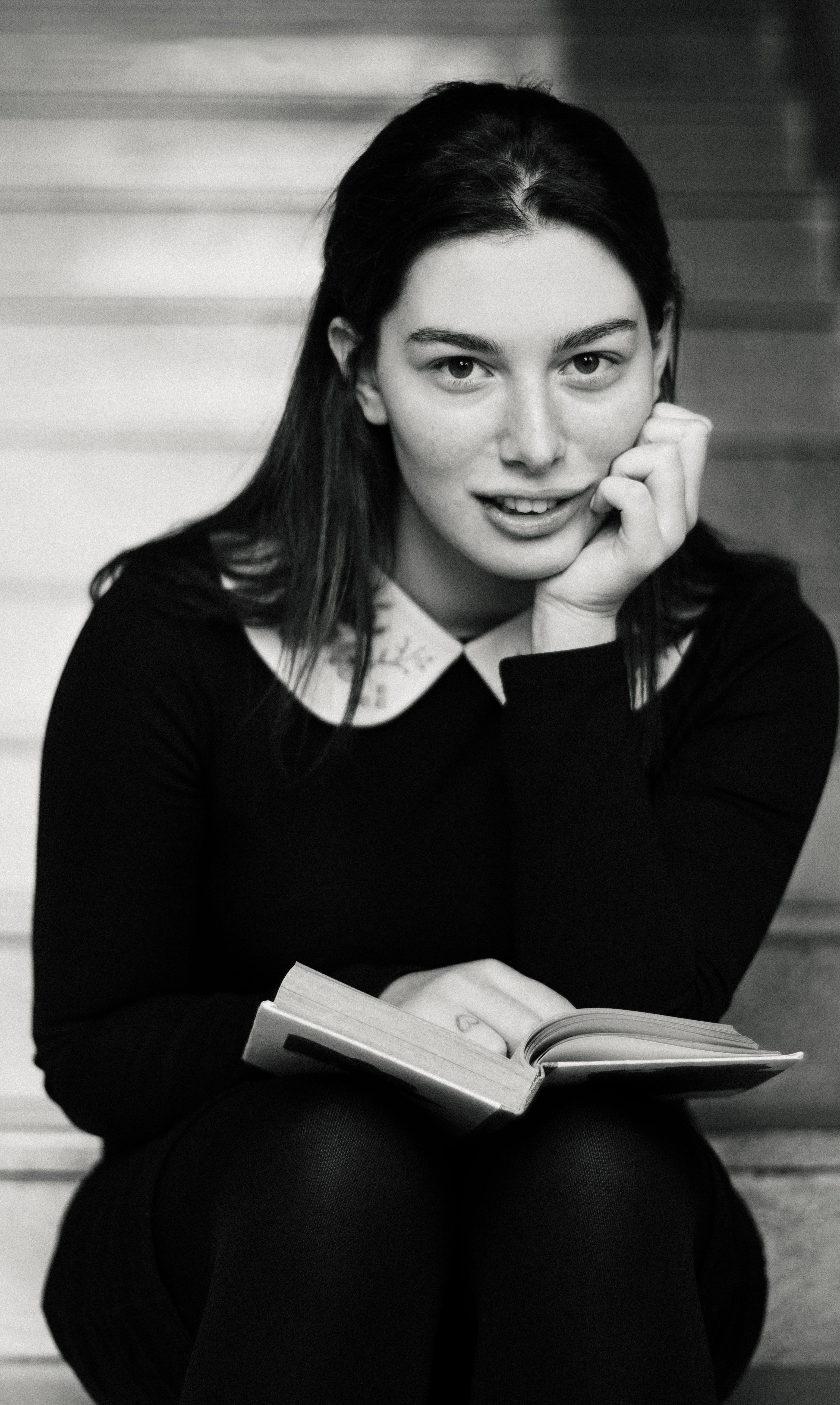 Striking monochrome portrait of a young woman sitting on stairs, reading a book.
