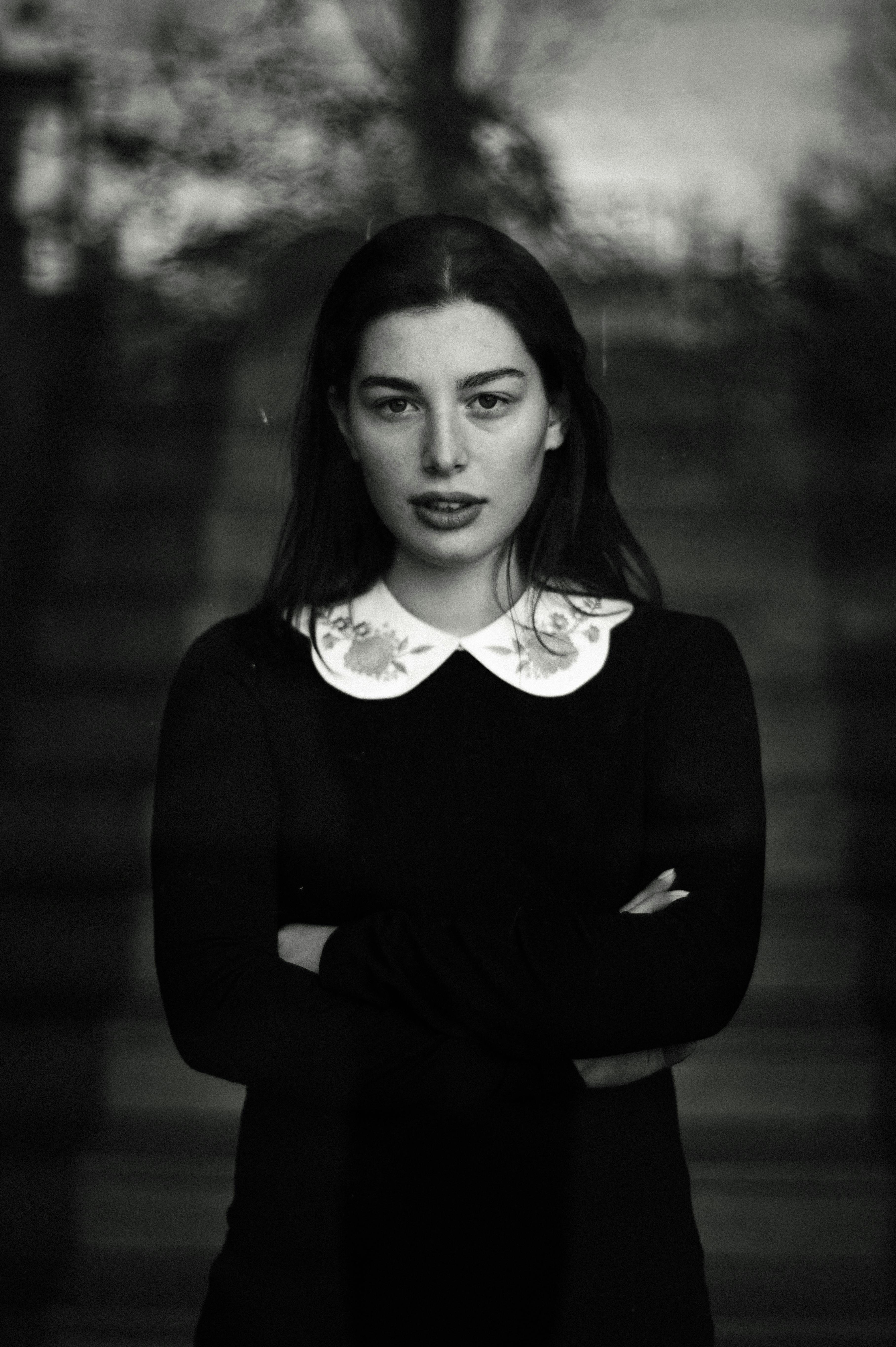 A striking black and white portrait of a woman with an intense gaze, arms crossed, and vintage style.