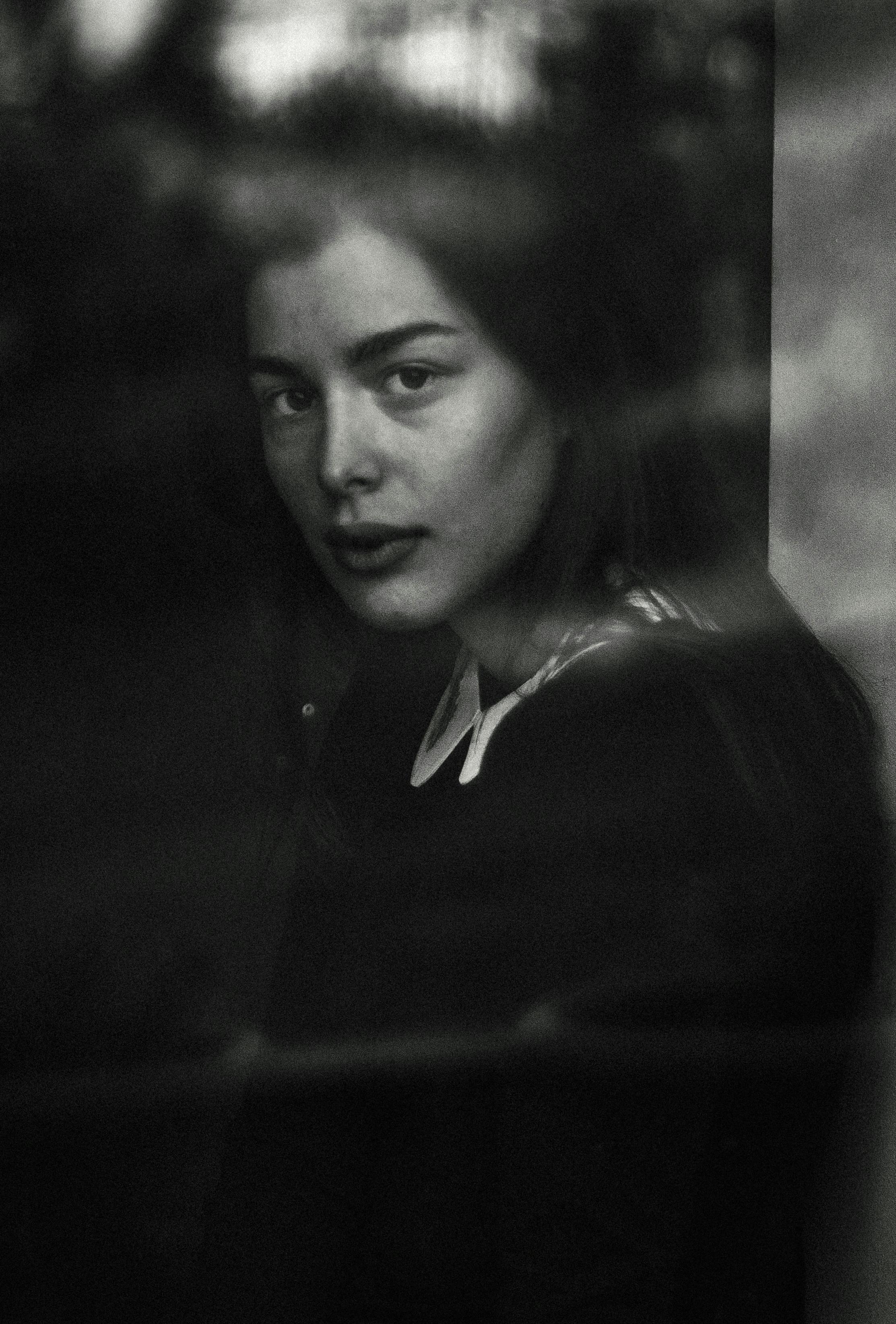 Intriguing monochrome portrait of a woman looking through glass, evoking deep emotions.