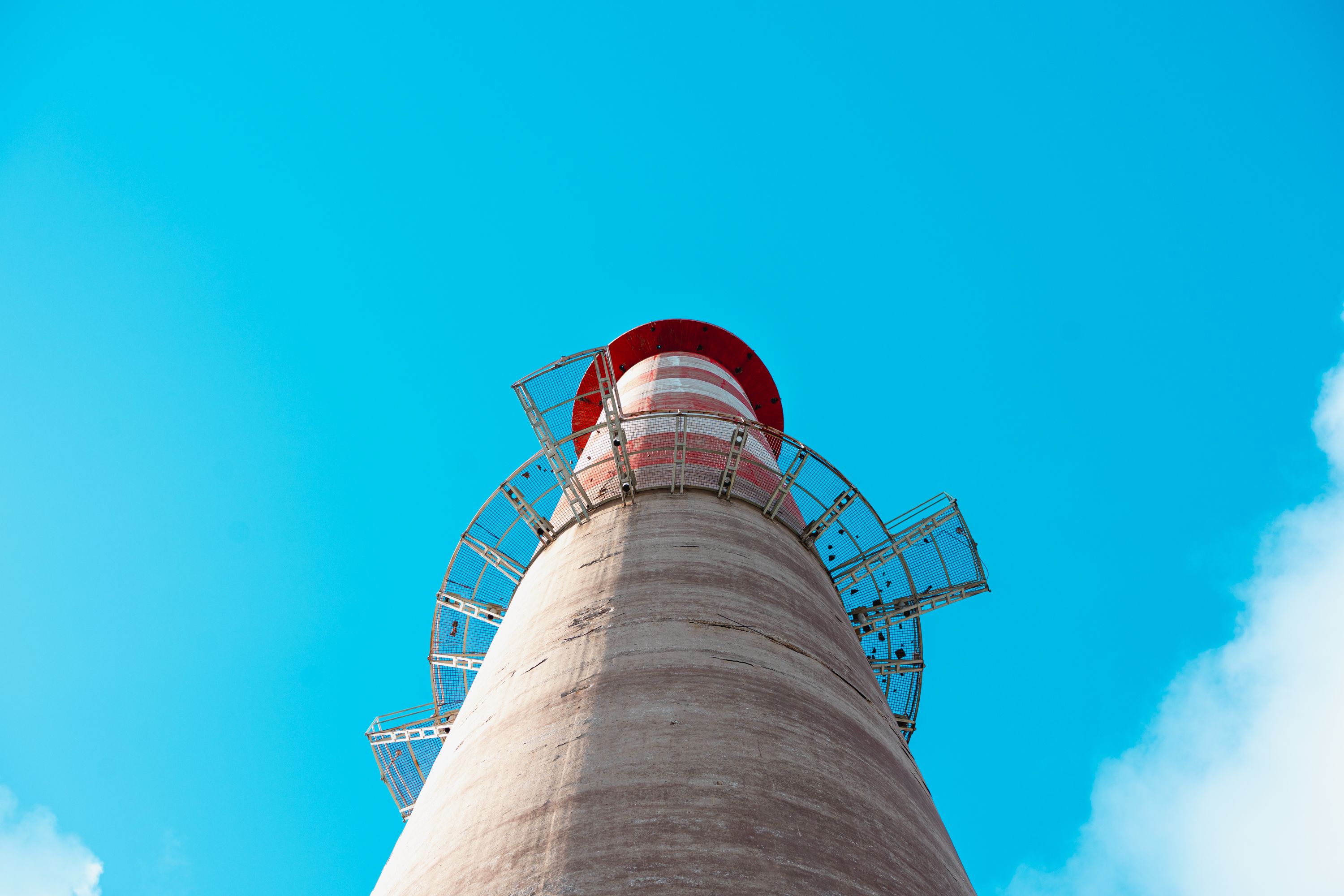 Striking upward shot of a tower with metal structures against a bright blue sky, featuring a vivid red accent.
