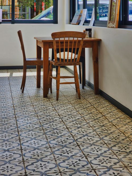 Free Charming cafe corner featuring wooden chairs, a table, and decorative tiles in a sunlit room. Stock Photo