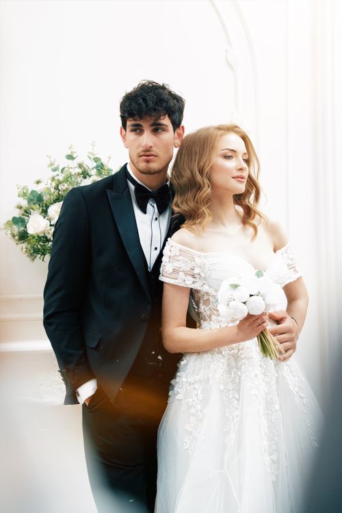 Free Stylish groom and bride in elegant attire, posing indoors. Perfect for wedding themes. Stock Photo