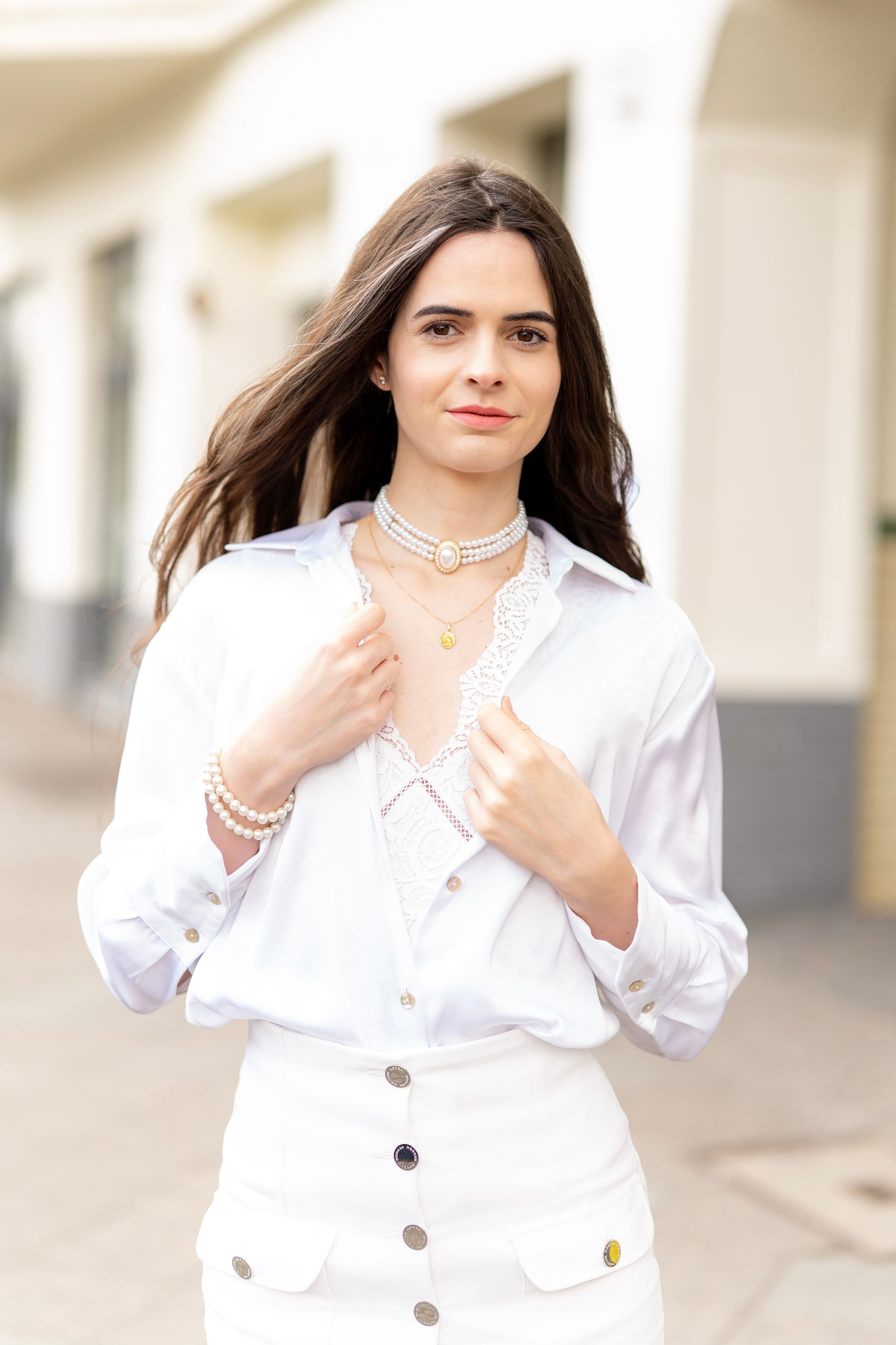 Elegant woman wearing white outfit and pearls, walking in Berlin.