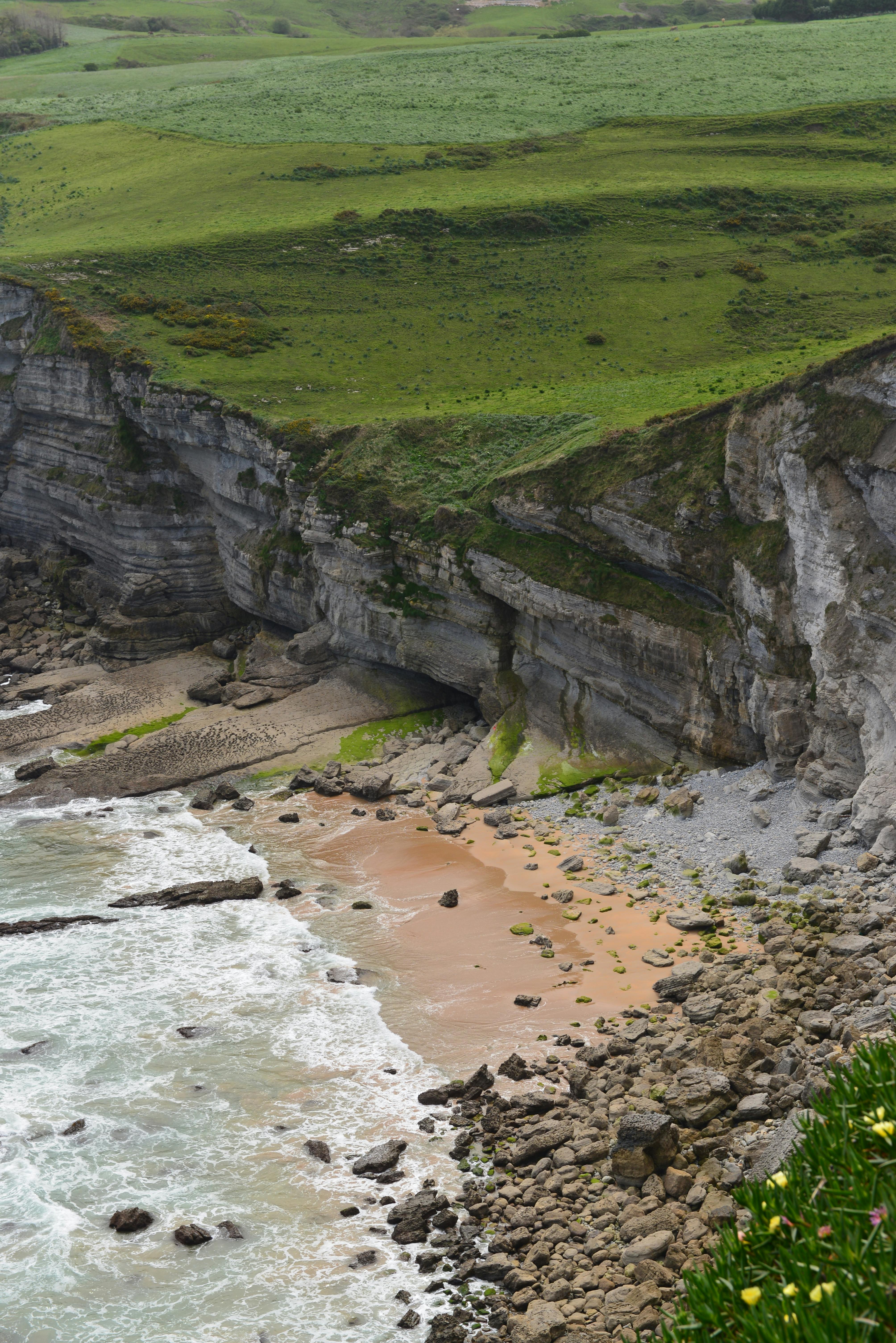 Dramatic coastal cliffs and beach in Tagle, Spain with lush greenery.