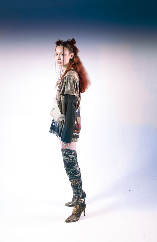 Free Young woman in stylish outfit and knee-high boots stands confidently in a well-lit studio setting. Stock Photo