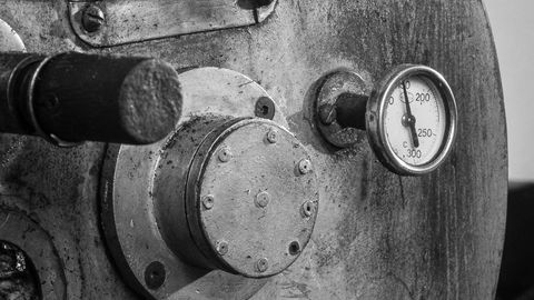 A detailed black and white image of an industrial coffee roaster machine, highlighting gauge and metal textures.
