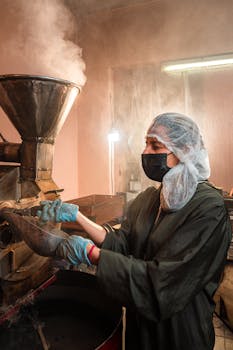Worker in protective gear operating coffee roasting machinery, ensuring quality control.