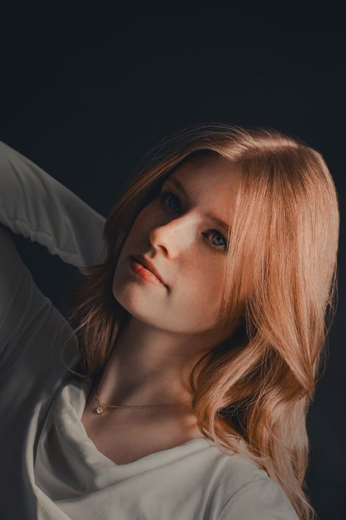 Free Artistic portrait of a woman with red hair and soft expression against a dark backdrop. Stock Photo