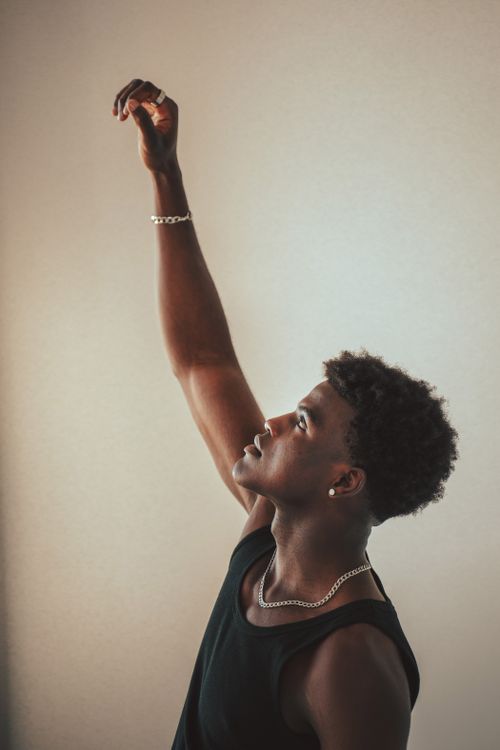 Free A young black man in a black tank top reaches upwards, expressing confidence and aspiration. Stock Photo