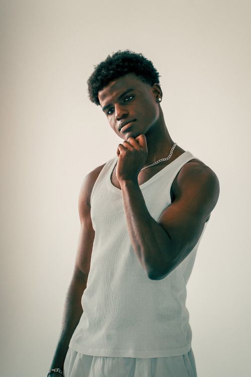 Free Portrait of a young man wearing a white tank top, standing indoors with confident expression. Stock Photo