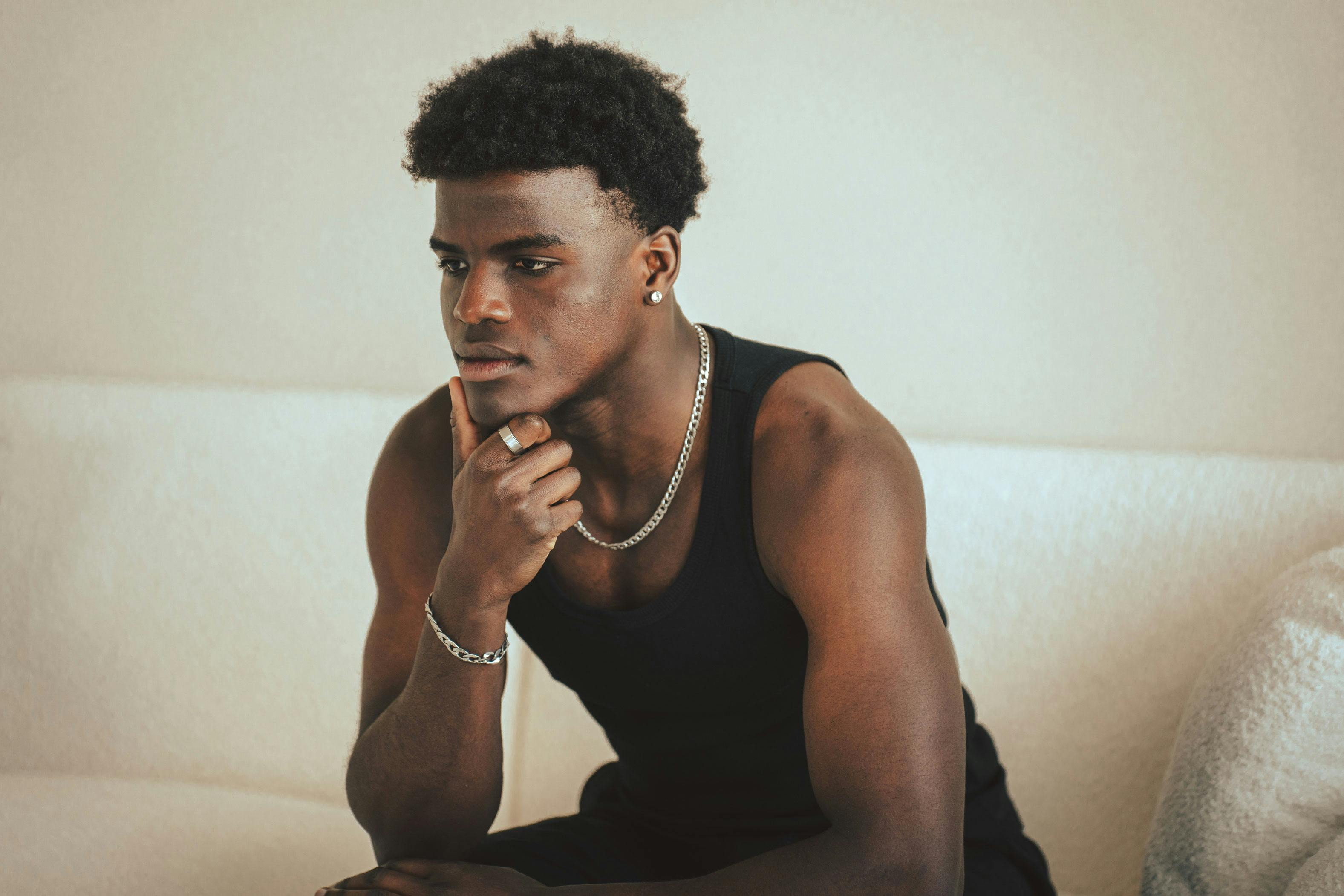 Young man sitting thoughtfully on a sofa indoors, exuding a calm and introspective vibe.