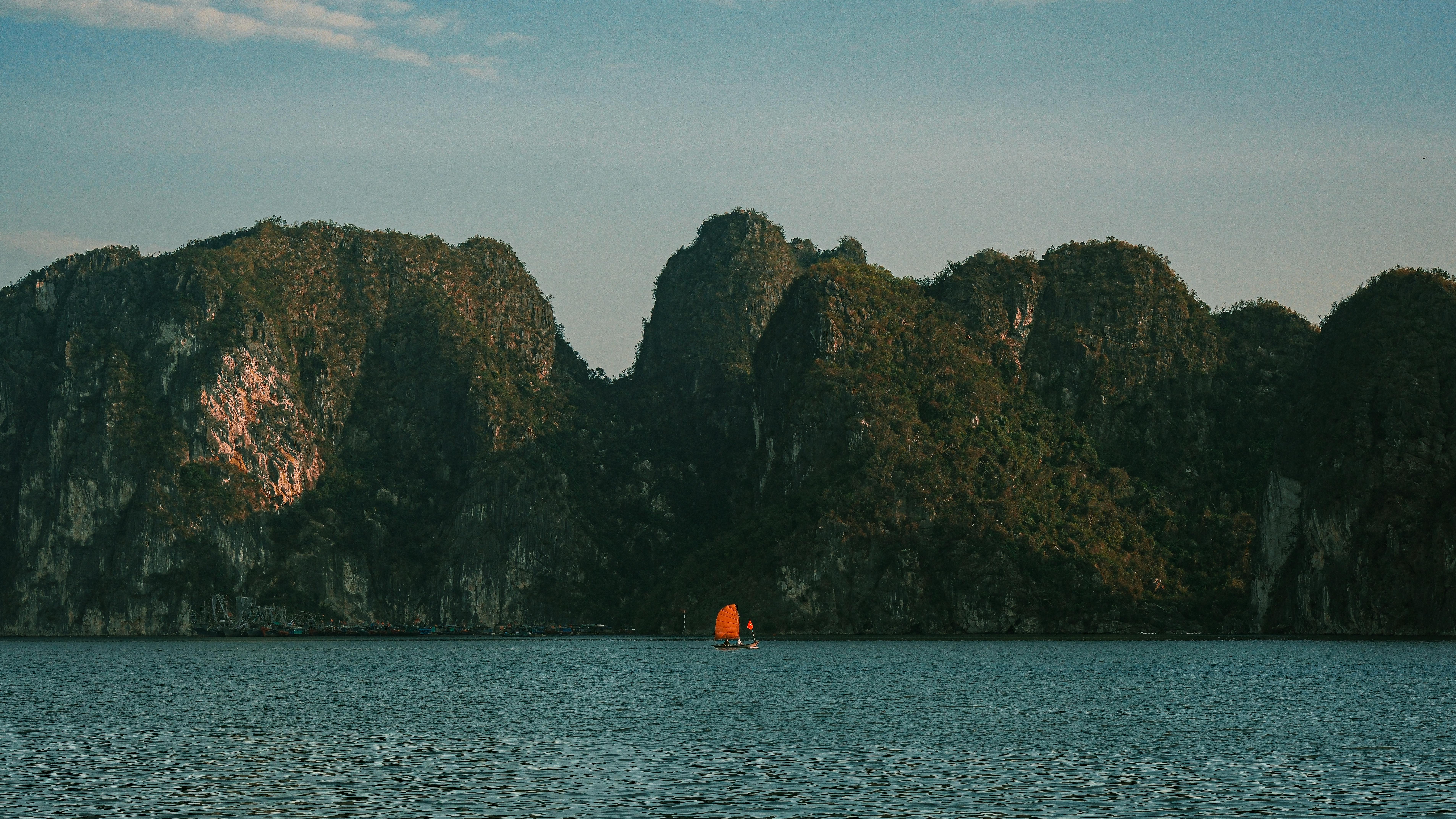Serene image of limestone mountains with a small boat on tranquil water under a blue sky.