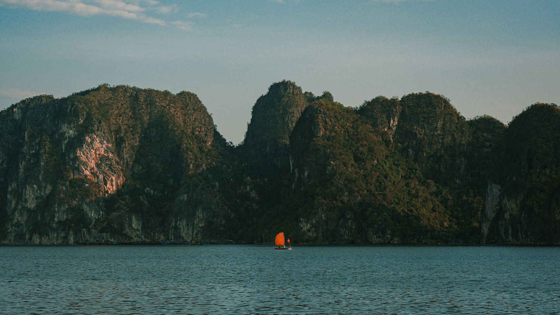 Serene image of limestone mountains with a small boat on tranquil water under a blue sky.