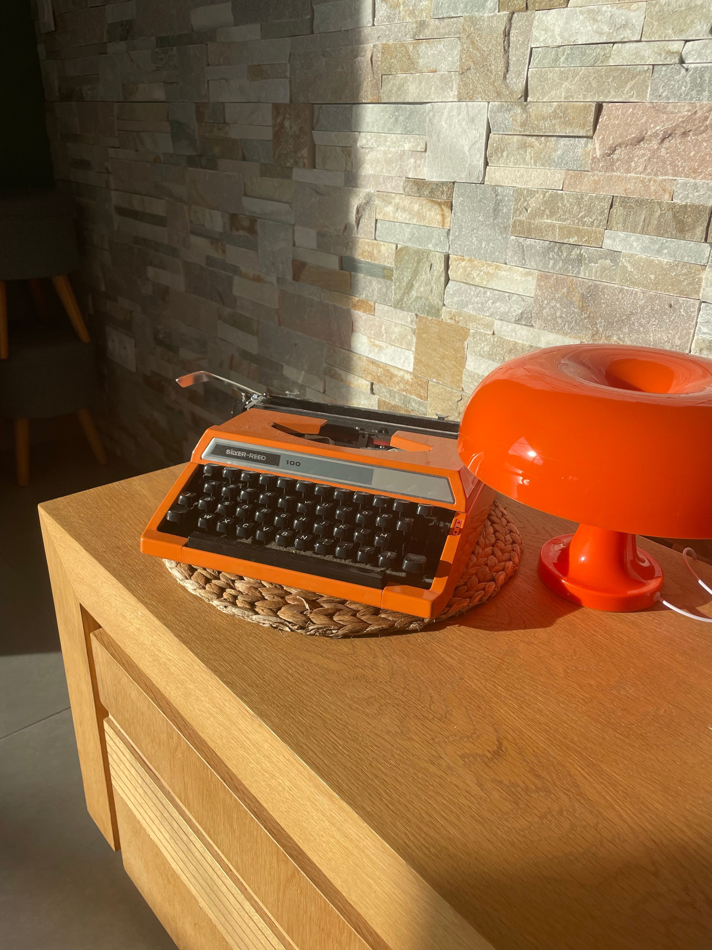 A vintage orange typewriter and retro lamp sit on a wooden desk, bathed in sunlight, adding a nostalgic flair.