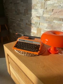 A vintage orange typewriter and retro lamp sit on a wooden desk, bathed in sunlight, adding a nostalgic flair.