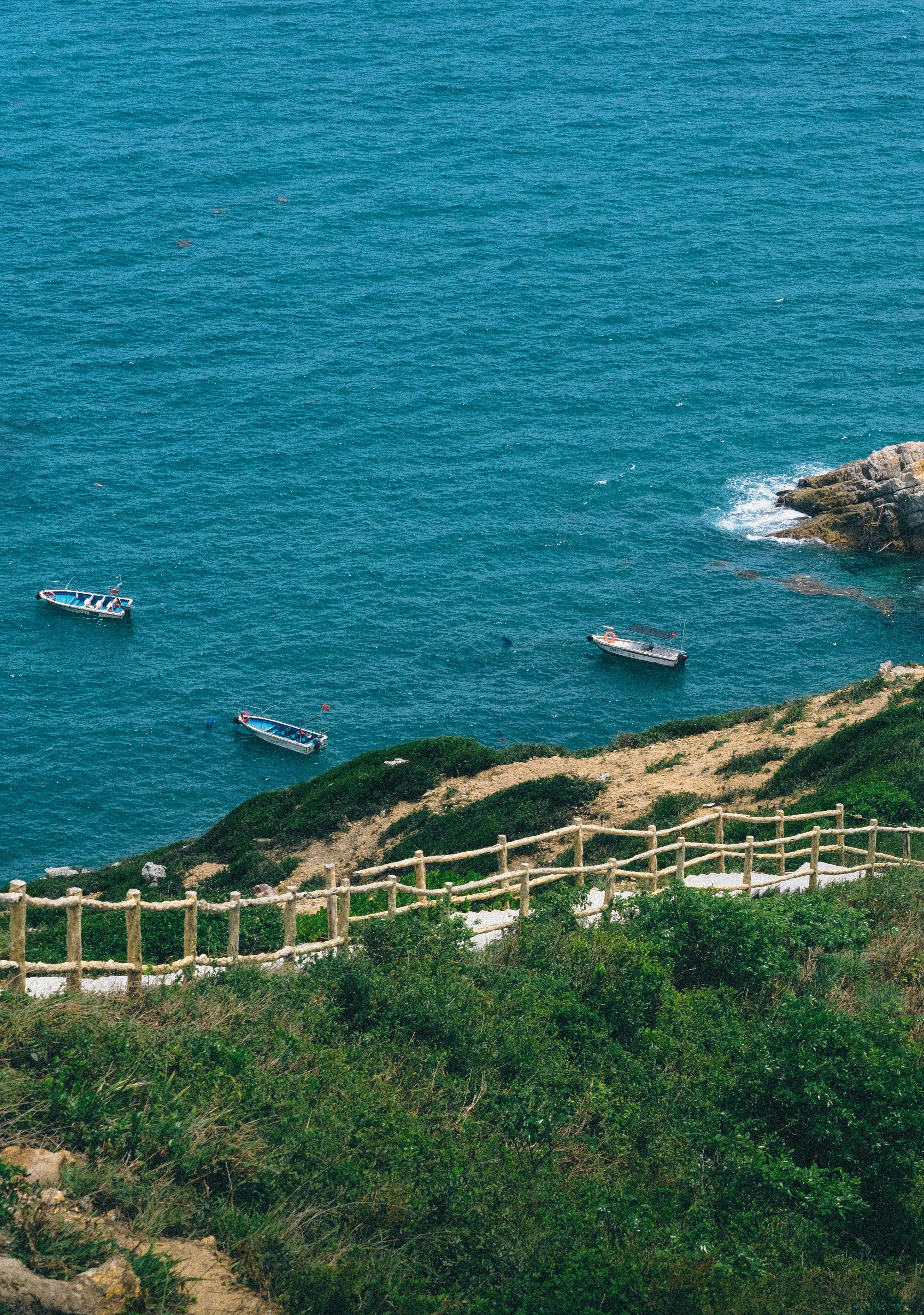 Idyllic coastal landscape with clear blue waters and small boats along a cliffside path.