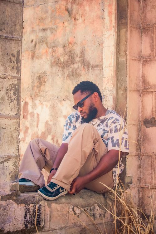 Free A man in sunglasses sits contemplatively against a rustic wall, embodying relaxation. Stock Photo