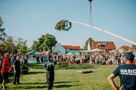 A vibrant outdoor community festival featuring a maypole and a lively crowd under clear skies.