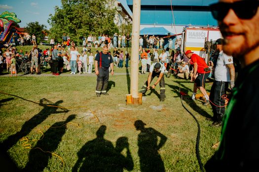 A vibrant summer festival with people gathered around a pole-raising event outdoors.