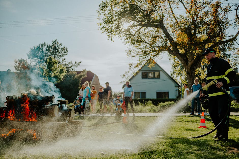 A firefighter extinguishes a controlled fire as a crowd watches during a demonstration on a sunny day.