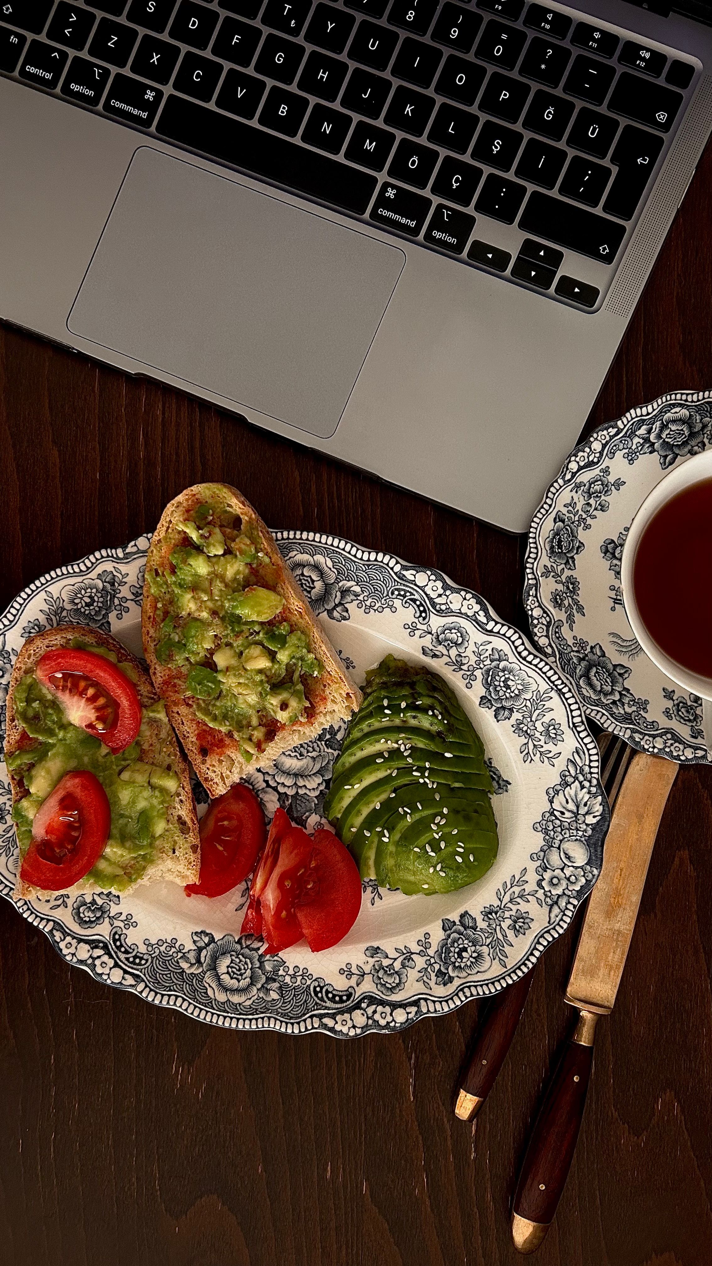 Top view of avocado toast and tea beside a laptop, perfect for a healthy and productive brunch setup.